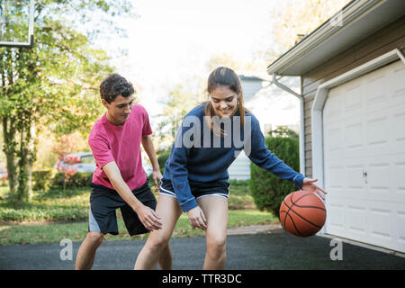 Happy brother and sister playing basketball at backyard Stock Photo