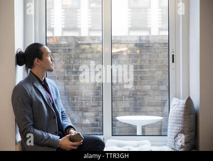 Thoughtful man looking through window while sitting in office Stock Photo