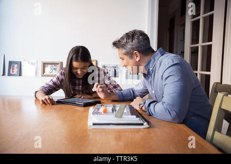 Father and daughter using tablet computer while sitting at table Stock Photo