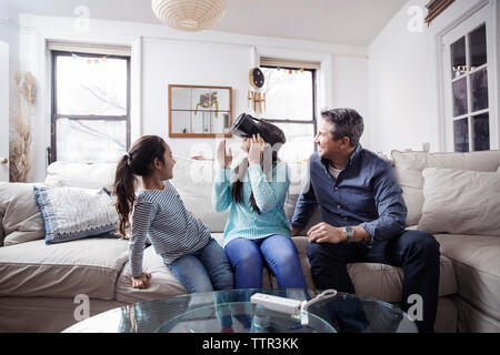 Father and daughter looking at girl wearing virtual reality simulator while sitting on sofa Stock Photo