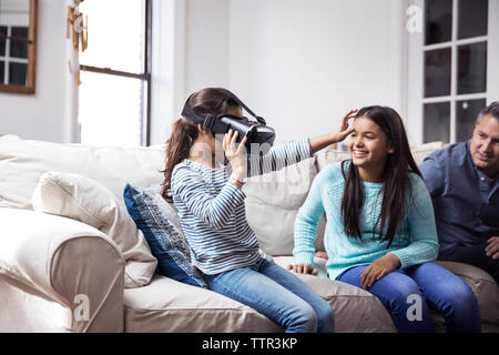 Father and daughter looking at girl wearing virtual reality simulator while sitting at home Stock Photo