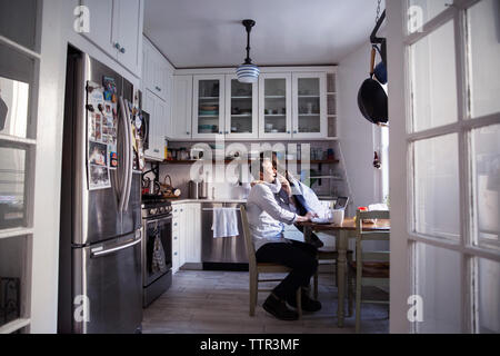 Daughter embracing father using laptop computer in kitchen at home Stock Photo