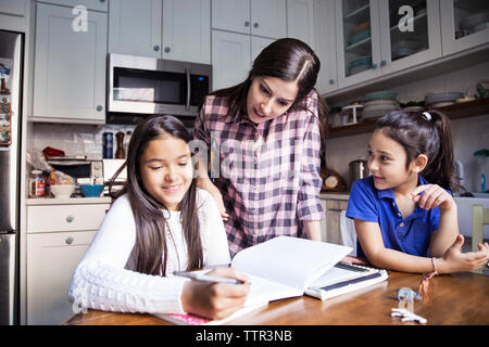 Mother looking girl studying in kitchen Stock Photo