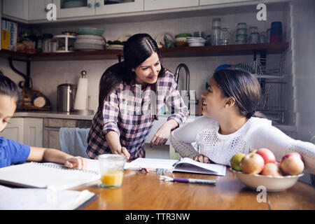 Mother talking to daughter studying at table in kitchen Stock Photo