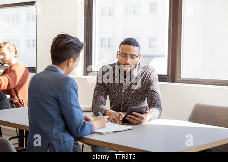 businessman showing tablet computer to female colleague at table in office Stock Photo