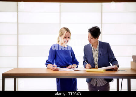 Female colleagues discussing while standing at table in office Stock Photo