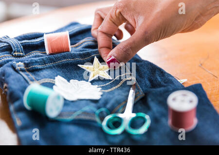 Cropped hand of woman putting star shape textile patch on jeans at table Stock Photo