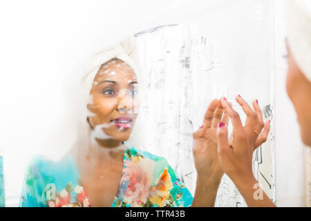 Woman wearing towel on head while looking at reflection in mirror Stock Photo