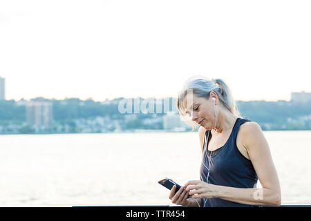 Woman using smart phone while listening music on bridge against clear sky Stock Photo