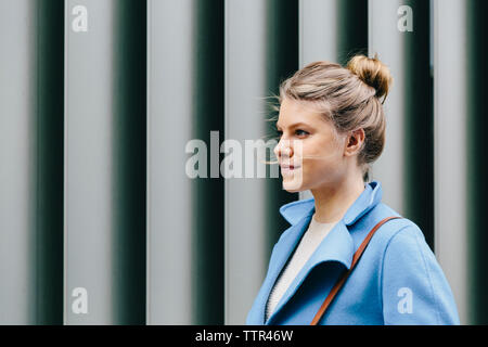 Confident young woman wearing trench coat while looking at river by ...