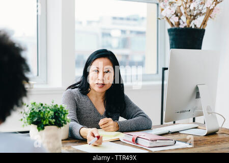 businesswoman talking with female colleague while working at desk in office Stock Photo