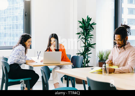 businessman reading documents while female colleagues discussing over laptop computer in office Stock Photo