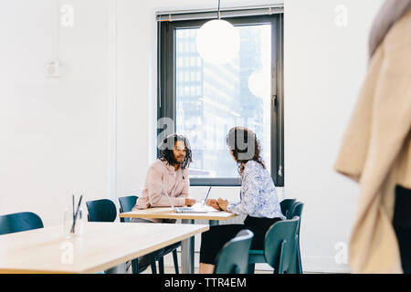 businesswoman discussing with businessman while sitting at desk in office Stock Photo