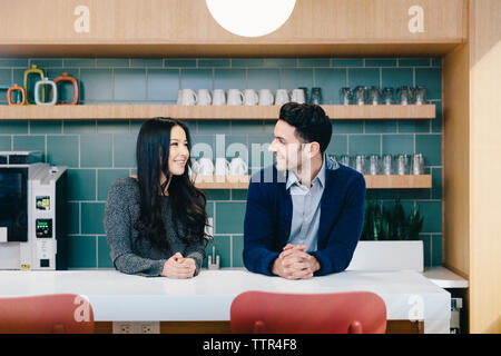 Colleagues talking while standing by table in cafeteria at creative office Stock Photo