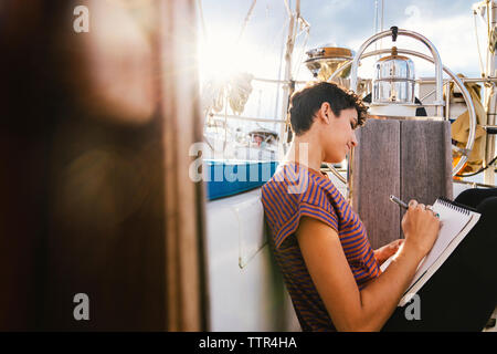 Side view of woman writing while sitting on book in boat seen through window Stock Photo