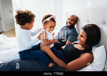Happy parents playing with children while relaxing on bed at home Stock Photo