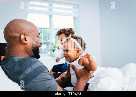 Happy father playing with children while relaxing on bed at home Stock Photo