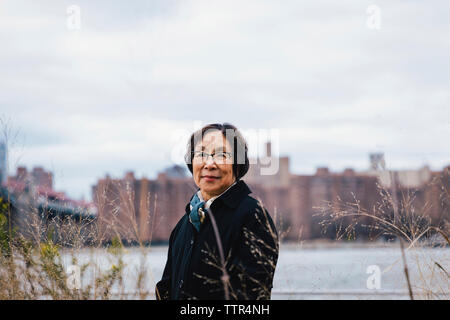 Portrait of smiling senior woman standing against cloudy sky in city