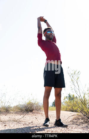 Low angle view of male hiker with arms raised exercising while standing on field against clear sky Stock Photo