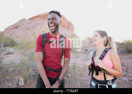 Happy friends with backpacks laughing while standing against rock formations Stock Photo