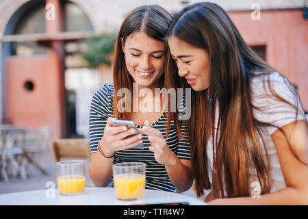 Friends using mobile phone while sitting at sidewalk cafe Stock Photo