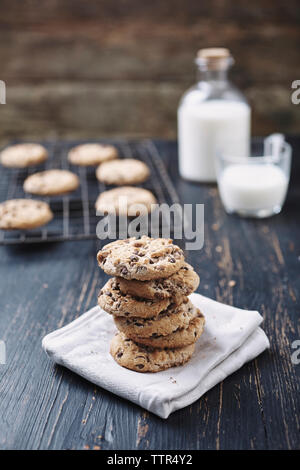 Stack of chocolate chip cookies with milk in background on wooden table Stock Photo