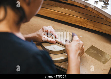 High angle view of female artisan measuring ring on wooden table in workshop Stock Photo