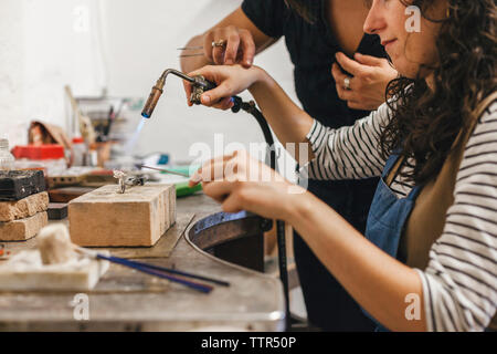 Midsection of female teacher assisting student in using blow torch on ring at workshop Stock Photo