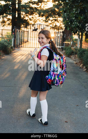 Side view of happy schoolgirl with backpack waving