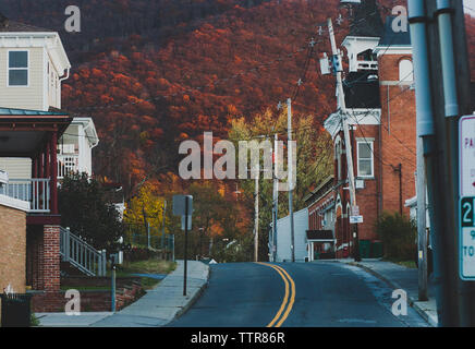 Empty road amidst buildings against trees on mountain in city during autumn Stock Photo