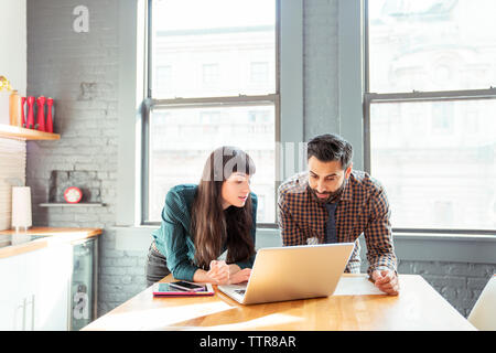 Man and woman using laptop computer while standing at table in office Stock Photo