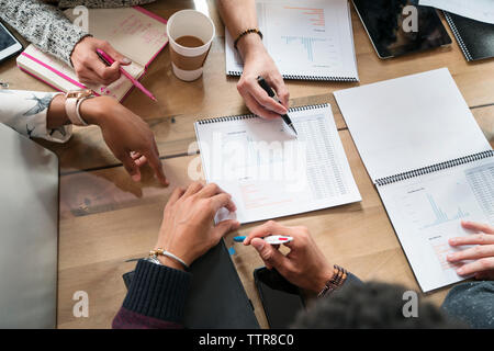 Cropped image of colleagues discussing graphs at table in office Stock Photo