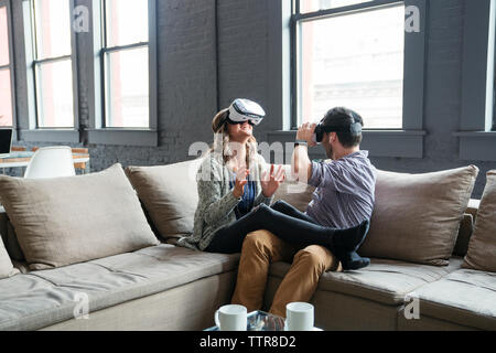 Happy business people wearing virtual reality simulator while sitting on sofa in office Stock Photo