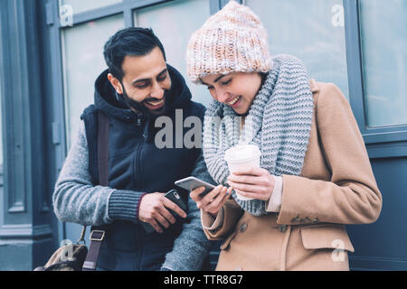 Happy couple using mobile phone while leaning by building in city Stock Photo