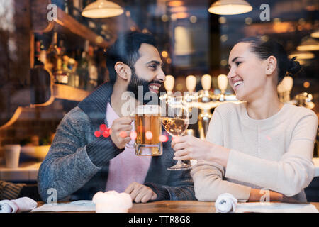 Happy couple toasting drinks seen through restaurant window Stock Photo