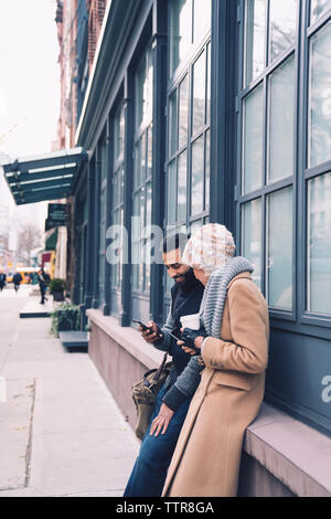 Couple using mobile phone while leaning by building in city Stock Photo