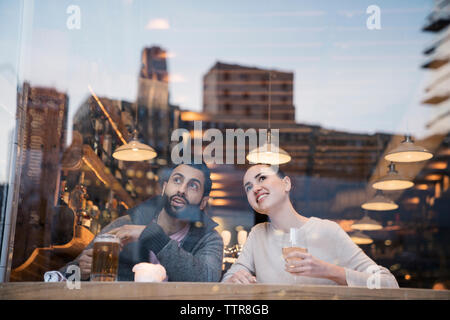 Couple enjoying drinks while looking away seen through restaurant window Stock Photo