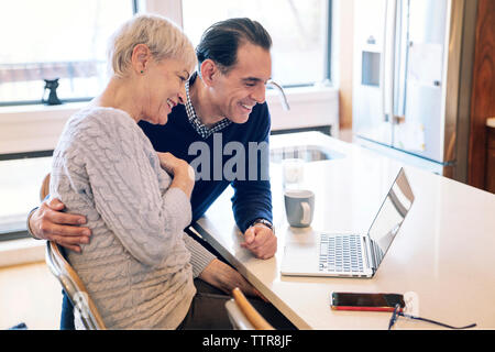 Smiling senior couple looking at laptop computer while sitting by table Stock Photo