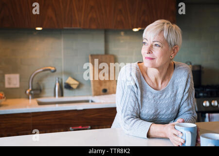 Thoughtful senior woman looking away while leaning on table Stock Photo