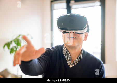 Smiling man pointing while wearing virtual reality simulator at home Stock Photo