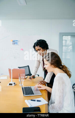 Female colleagues discussing over laptop computer in board room at office Stock Photo