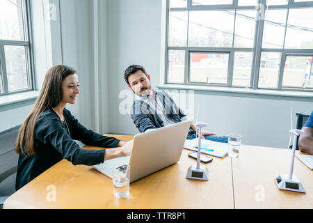 businesswoman showing laptop computer to colleague while sitting in board room Stock Photo