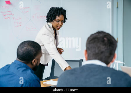 businesswoman discussing with male colleagues while standing in office Stock Photo