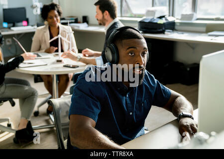 businessman using desktop computer while colleagues discussing in background Stock Photo