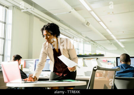 businesswoman using laptop computer while businessmen working in background Stock Photo