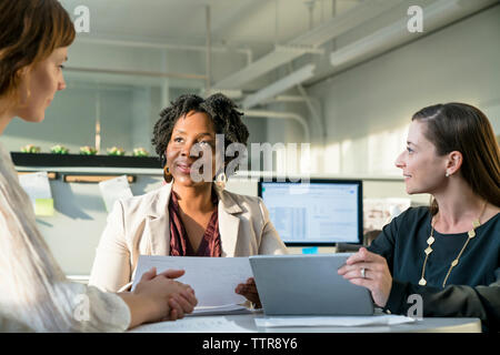 Smiling businesswomen discussing over tablet computer while sitting in office Stock Photo