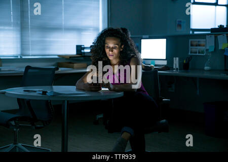 businesswoman using smart phone while sitting at table in office Stock Photo