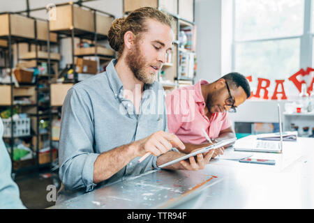 businessman using tablet computer while male colleague writing on paper at table Stock Photo