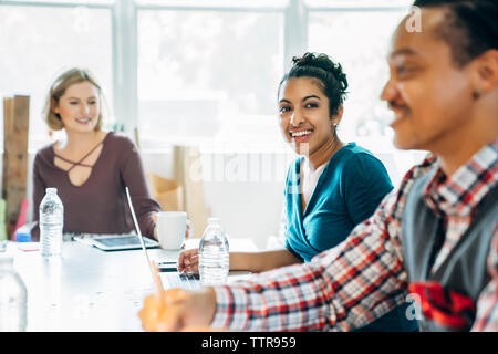 Happy businesswoman looking away while sitting by colleagues Stock Photo