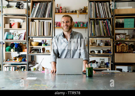 Portrait of happy businessman standing against racks in office Stock Photo